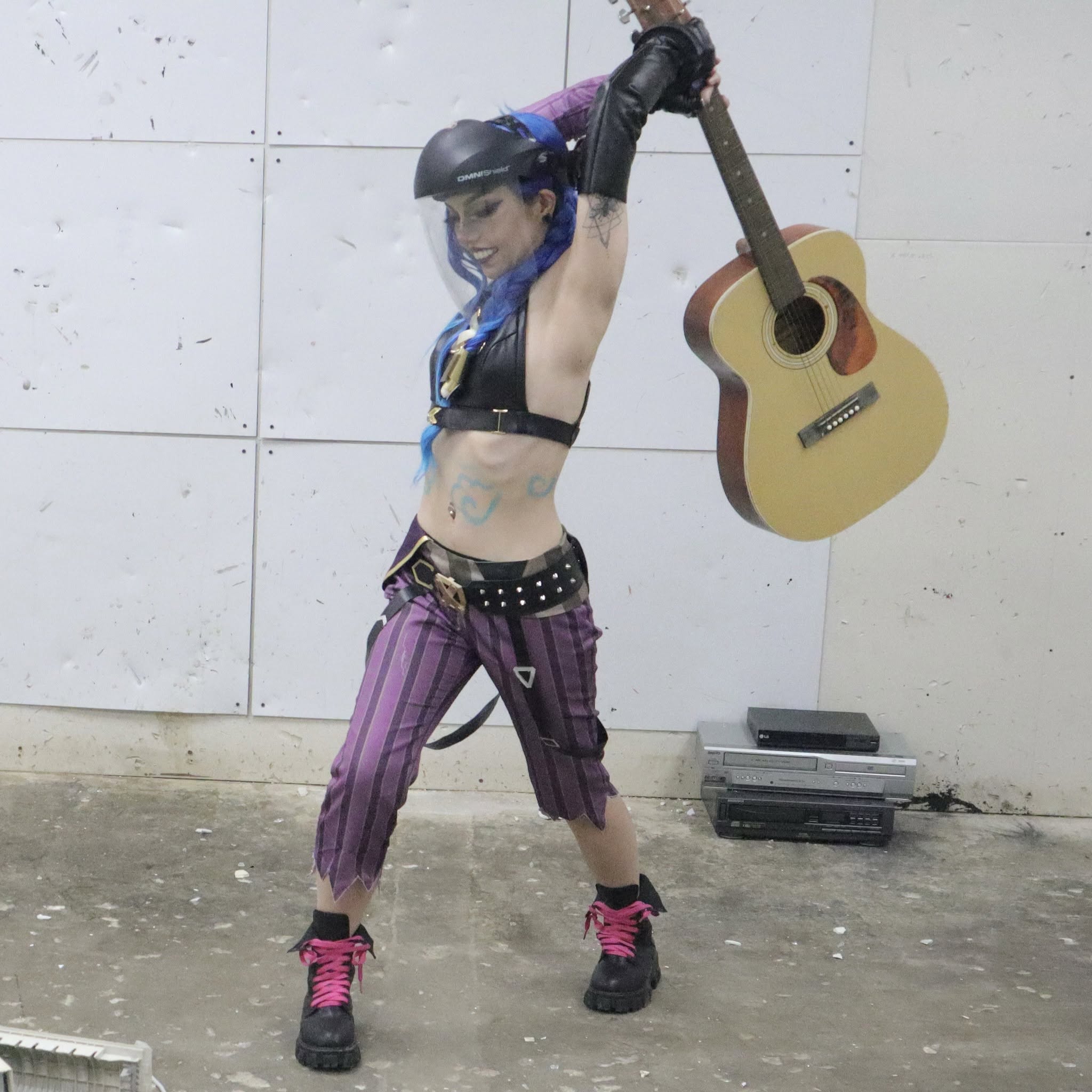 A guest in costume taking a big swing at a guitar in the rage room